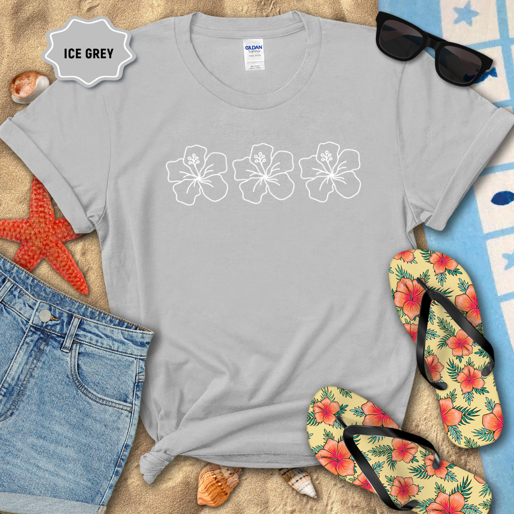 Gray t-shirt with floral designs on a sandy surface with beach accessories.