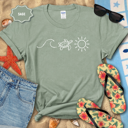 Sage green t-shirt with beach-themed design on sand with sunglasses, flip-flops, and starfish.