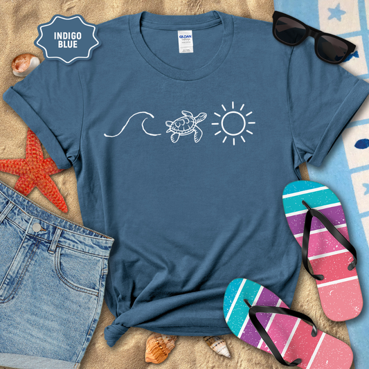 Indigo blue t-shirt with turtle and sun design on a beach setting with sunglasses, flip-flops, and starfish.