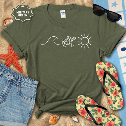 Military green t-shirt with turtle, wave, and sun design on a beach setting with sunglasses, flip-flops, and starfish.