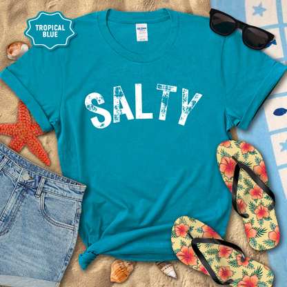Blue t-shirt with 'SALTY' text, sunglasses, flip-flops, and beach items on a sandy background.