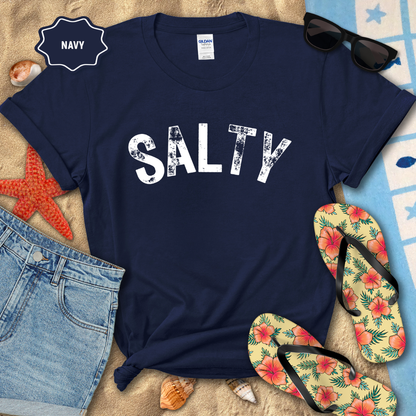 Navy t-shirt with 'SALTY' print on a beach-themed background with sunglasses, flip-flops, and denim shorts.