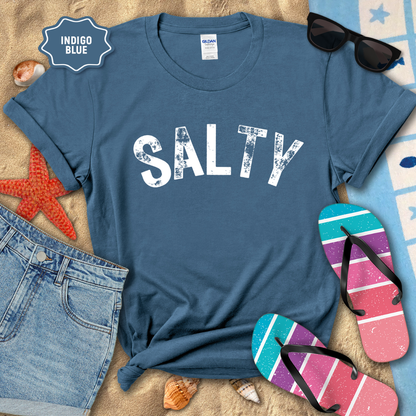 Indigo blue t-shirt with 'SALTY' text on a beach setting with sunglasses, flip-flops, and denim shorts.