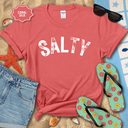 Coral t-shirt with 'SALTY' text on a beach setting with sunglasses, flip-flops, and starfish.