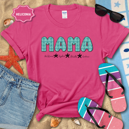 Pink t-shirt with 'MAMA' print on a sandy surface with beach accessories.
