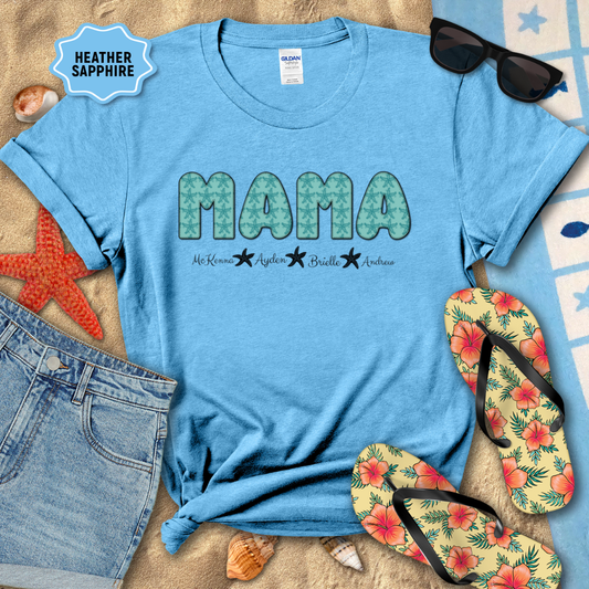 Blue t-shirt with 'MAMA' print on a sandy surface with beach accessories.