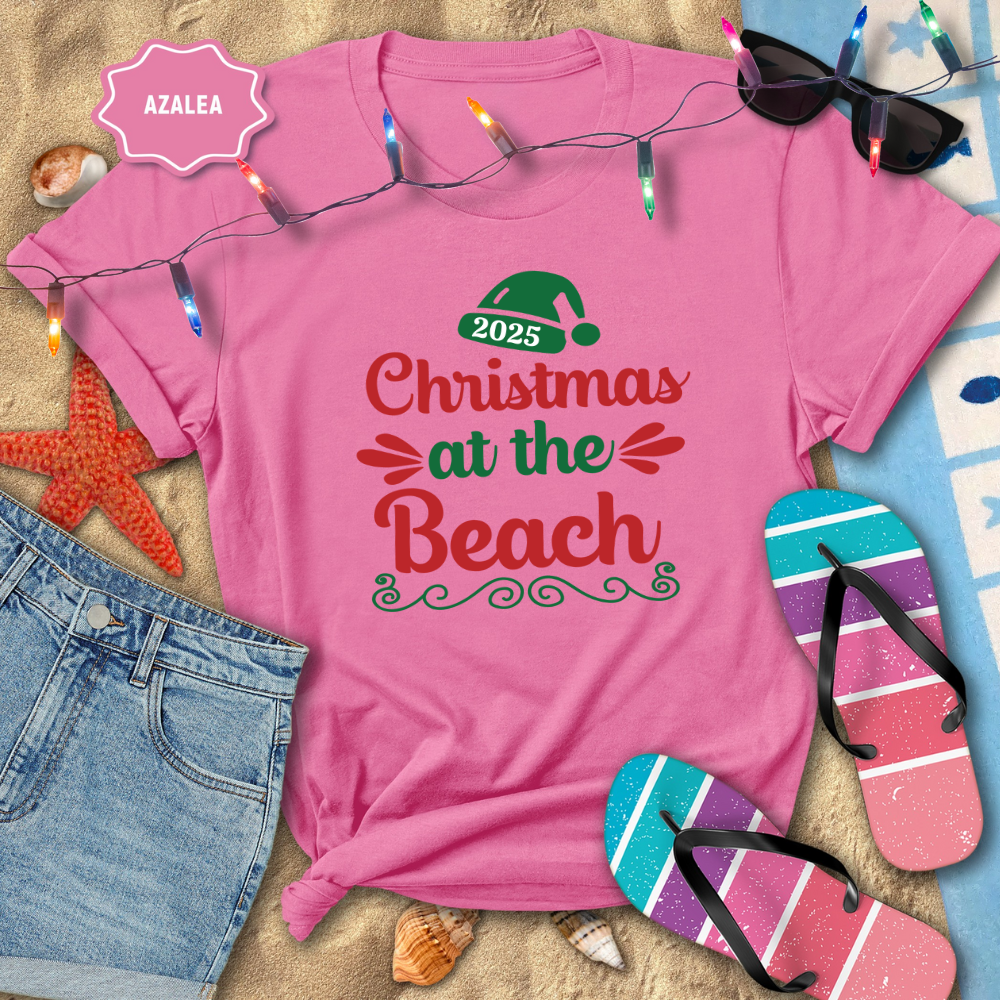 Pink t-shirt with 'Christmas at the Beach 2025' text, surrounded by beach-themed items like flip-flops and sunglasses.
