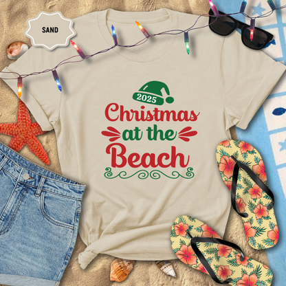 Beige t-shirt with 'Christmas at the Beach 2025' text, surrounded by beach-themed items like flip-flops and sunglasses.