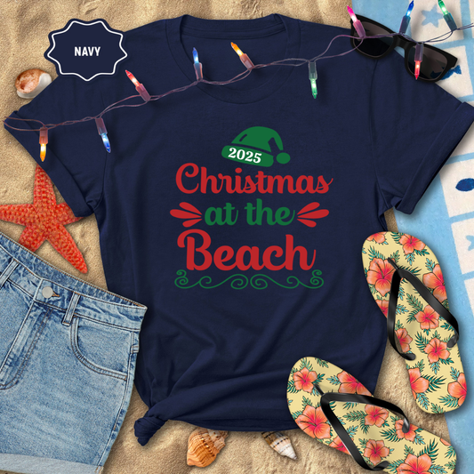 Navy t-shirt with 'Christmas at the Beach 2025' text, surrounded by beach-themed items like flip-flops and string lights.