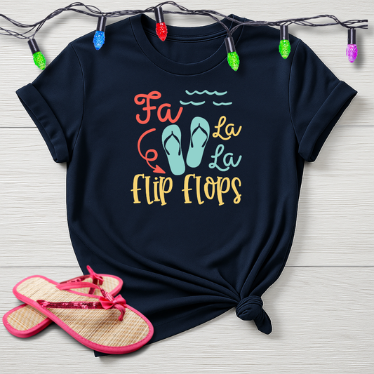 Black t-shirt with 'Fa La La La Flip Flops' design and pink sandals on a wooden surface.