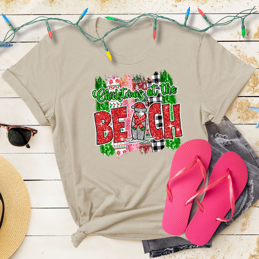 Beige t-shirt with 'Christmas at the Beach' design, pink flip-flops, and Christmas lights on a wooden surface.