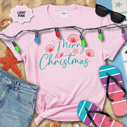 Light pink t-shirt with 'Merry Christmas' text and beach-themed decorations on a sandy background.