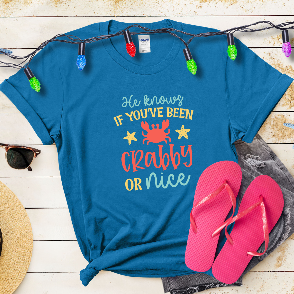 Blue t-shirt with humorous text design, pink flip-flops, and festive lights on a wooden surface.