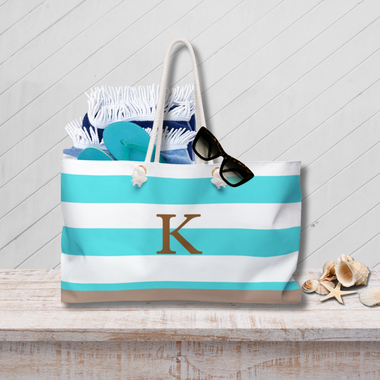 Striped beach bag with monogram 'K' on a wooden surface with beach accessories.