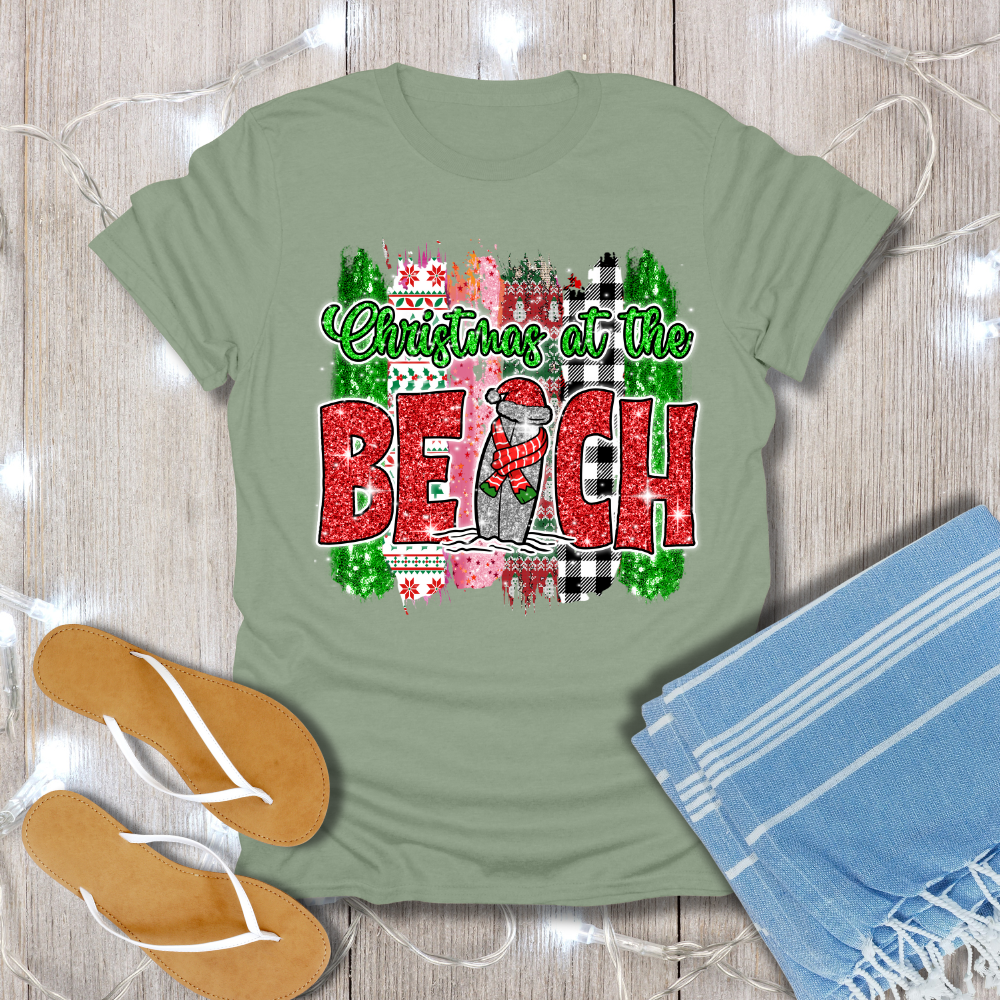 Green t-shirt with 'Christmas at the Beach' design on a wooden surface with flip-flops and a towel.