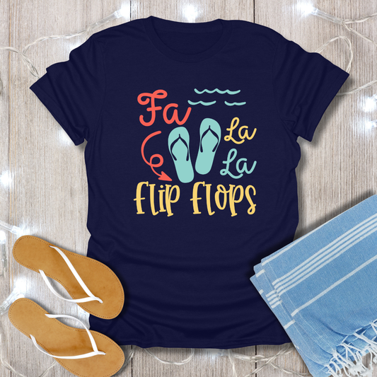 Navy blue t-shirt with 'Fa La La Flip Flops' text and sandals on a wooden surface.