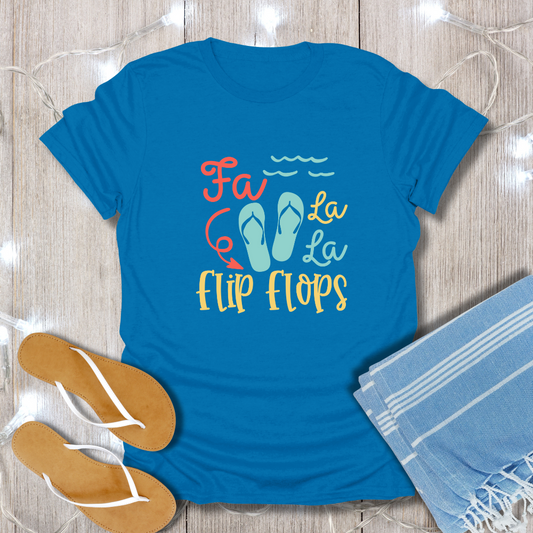 Blue t-shirt with 'Fa La La La Flip Flops' text and sandals on a wooden surface.