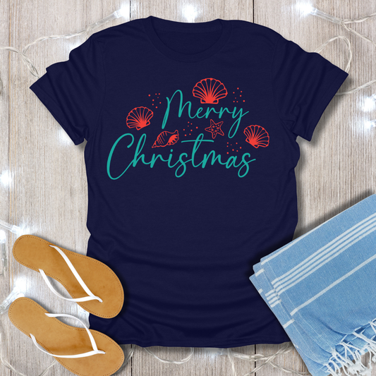 Navy blue t-shirt with 'Merry Christmas' text on a wooden surface with flip-flops and a towel.