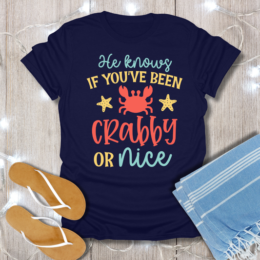 Navy blue t-shirt with a colorful graphic and text on a wooden surface with flip-flops and a towel.