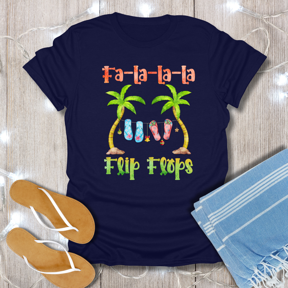 Navy blue t-shirt with 'Fa-la-la-la Flip Flops' design on a wooden surface with flip flops and a towel.