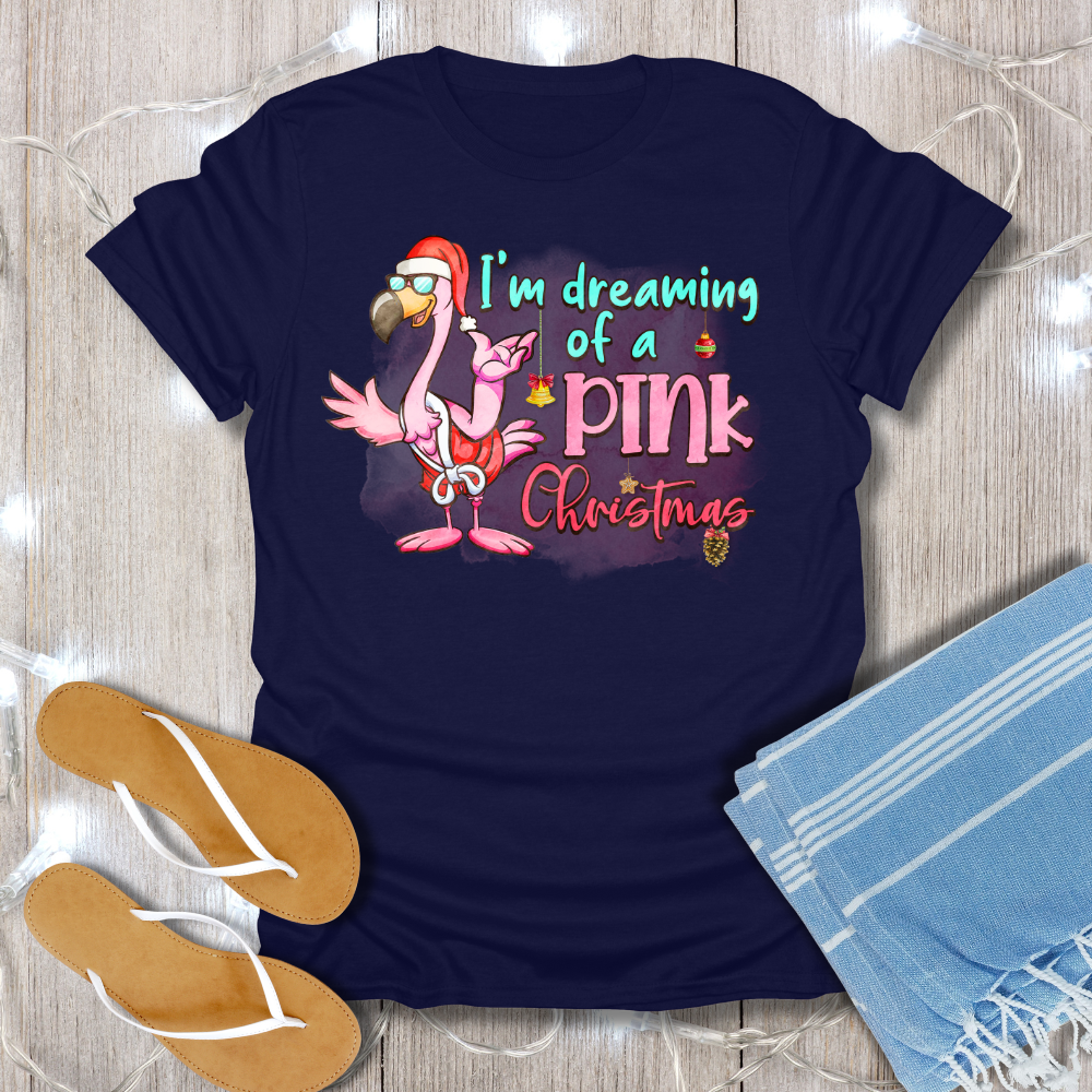 Navy blue t-shirt with flamingo graphic and text on a wooden surface with flip-flops and a towel.