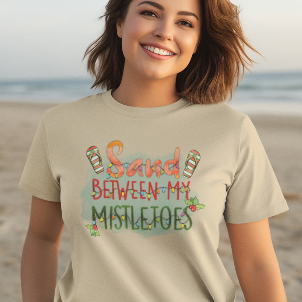 Woman wearing a t-shirt with 'Sand Between My Mistletoes' text on a beach