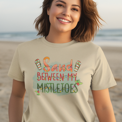 Woman wearing a t-shirt with 'Sand Between My Mistletoes' text on a beach