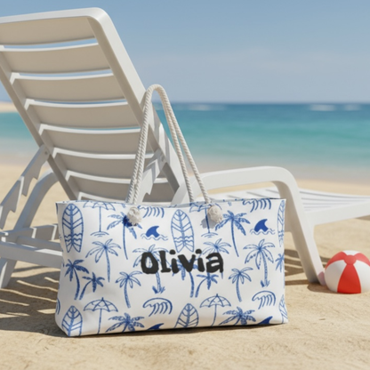 Beach bag with palm tree pattern and 'Olivia' branding on a sandy beach with a lounge chair and ball.