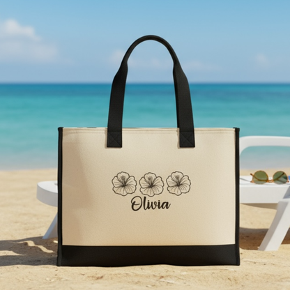 Beige tote bag with black handles and floral design on a beach