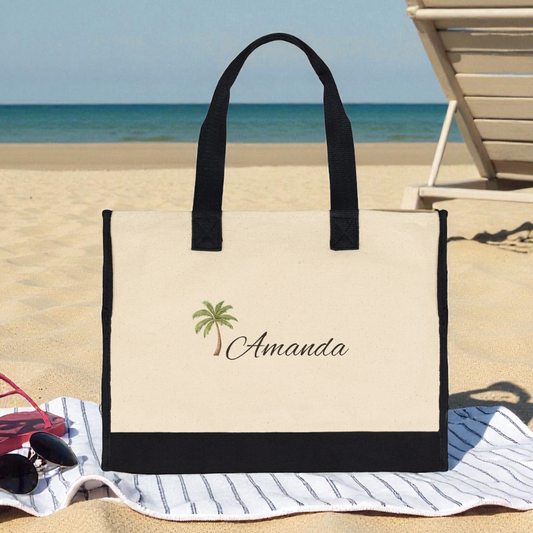 Beige tote bag with black handles and 'Amanda' and palm tree design on a beach.