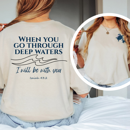 Person wearing a beige t-shirt with a motivational quote and wave design, sitting on a bed.