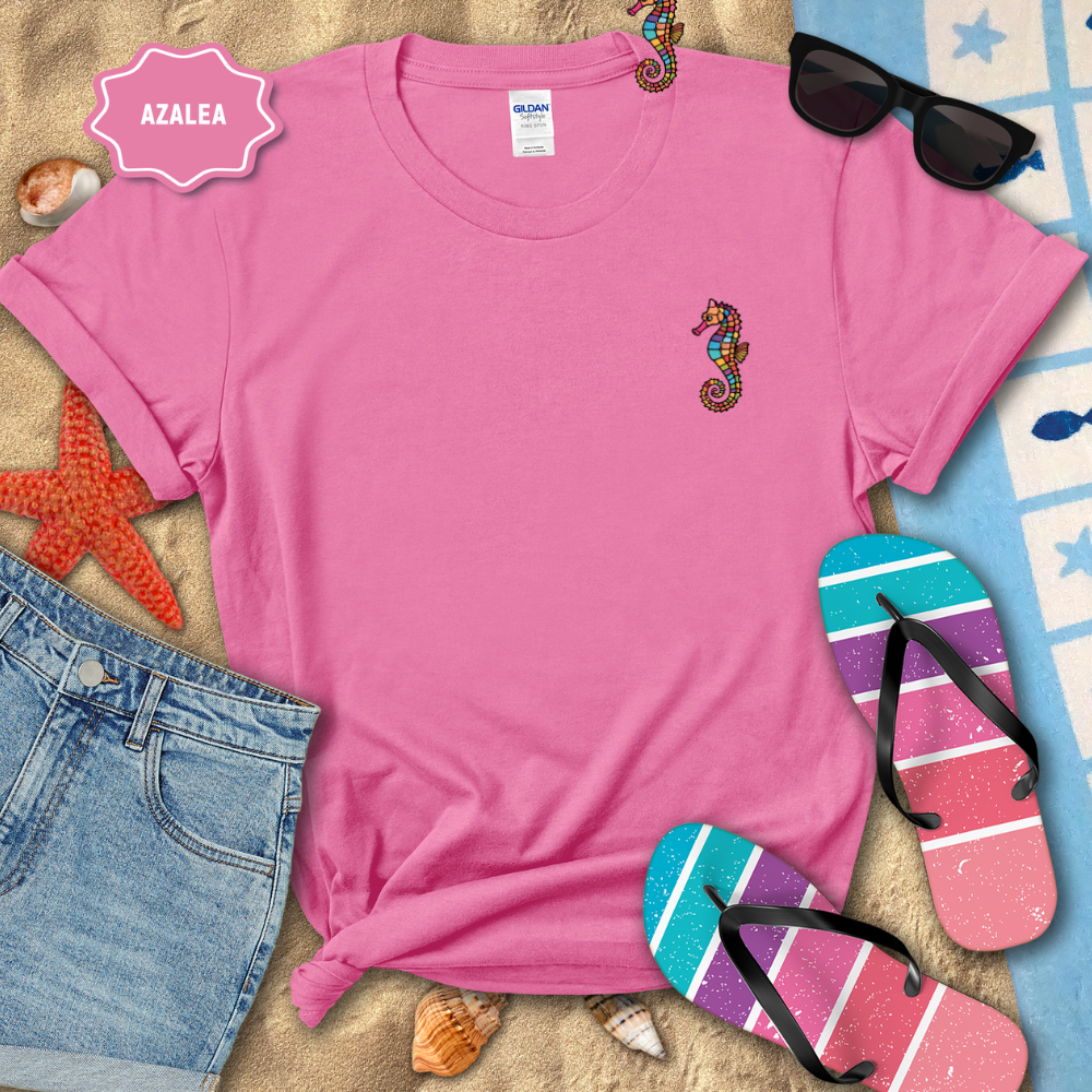 Pink t-shirt with seahorse design, sunglasses, and flip-flops on a beach-themed background.