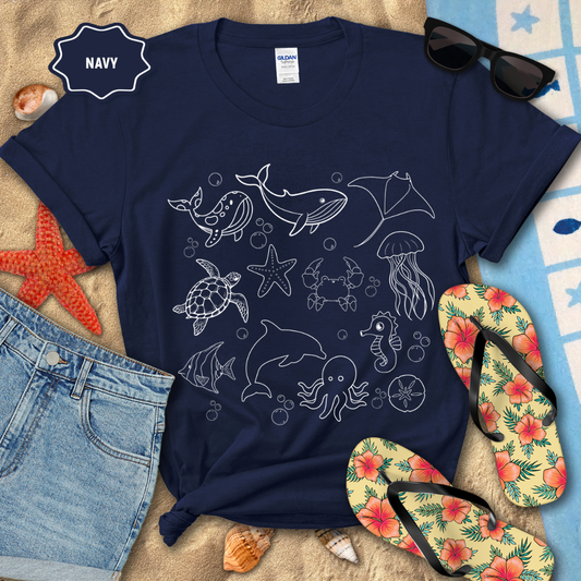 Navy t-shirt with marine animal designs on a beach setting with sunglasses, flip-flops, and beach accessories.