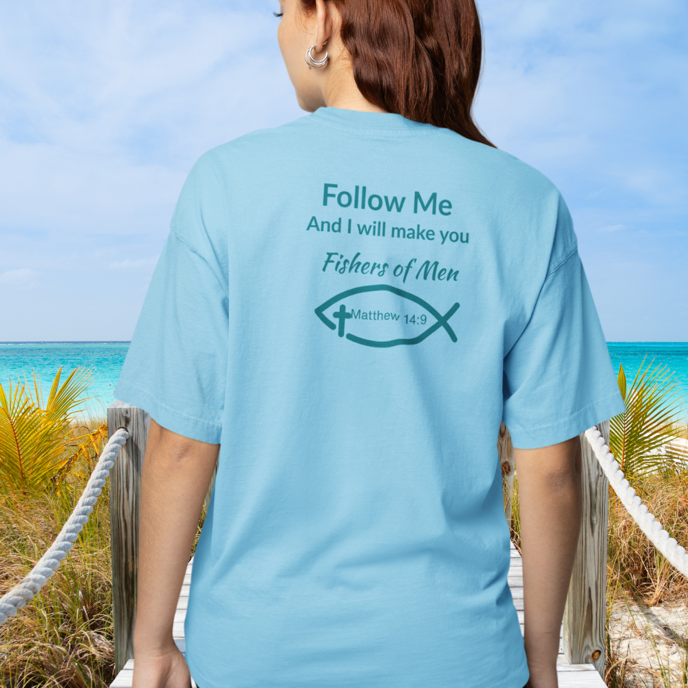 Person wearing a light blue t-shirt with a religious quote and design on the beach.