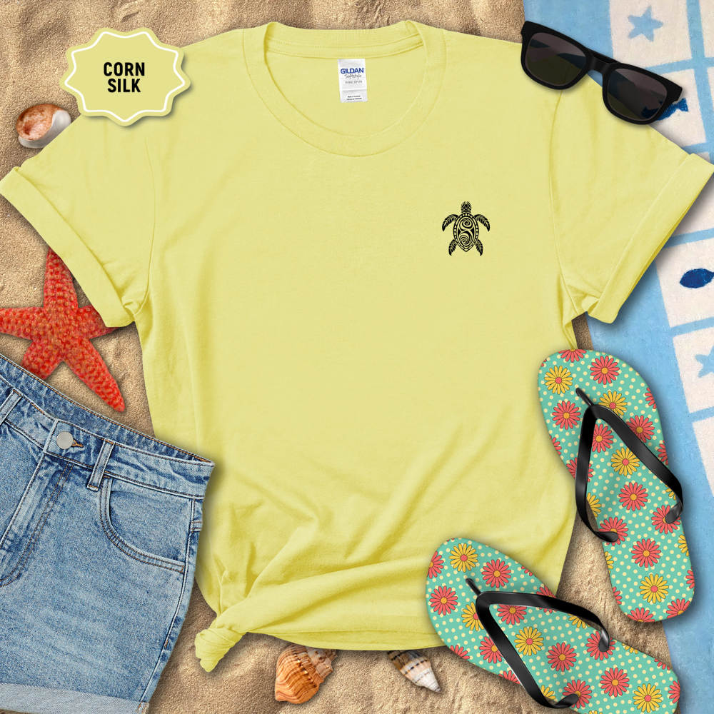 Yellow t-shirt with a turtle design on a sandy surface with flip-flops and sunglasses.