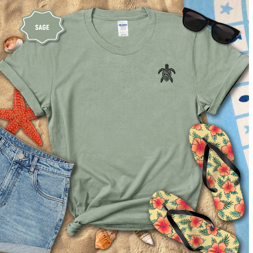 Sage green t-shirt with turtle design, sunglasses, floral flip-flops, and denim shorts on a sandy surface.