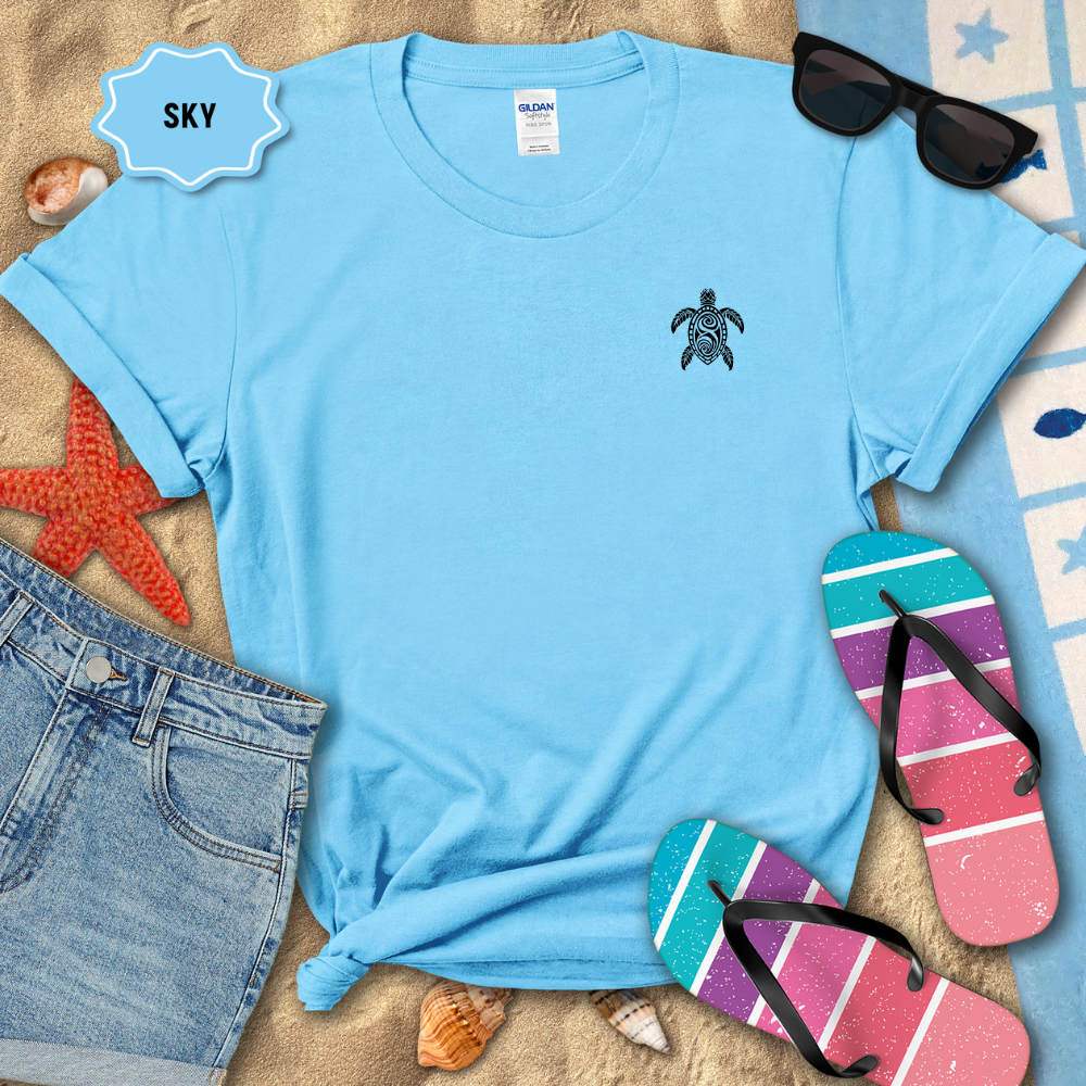 Blue t-shirt with a turtle logo on a sandy surface with beach accessories.