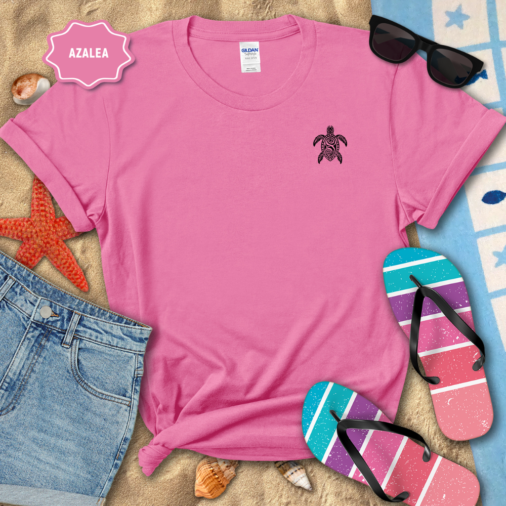 Pink t-shirt with a turtle design on a beach-themed background with sunglasses, flip-flops, and denim shorts.