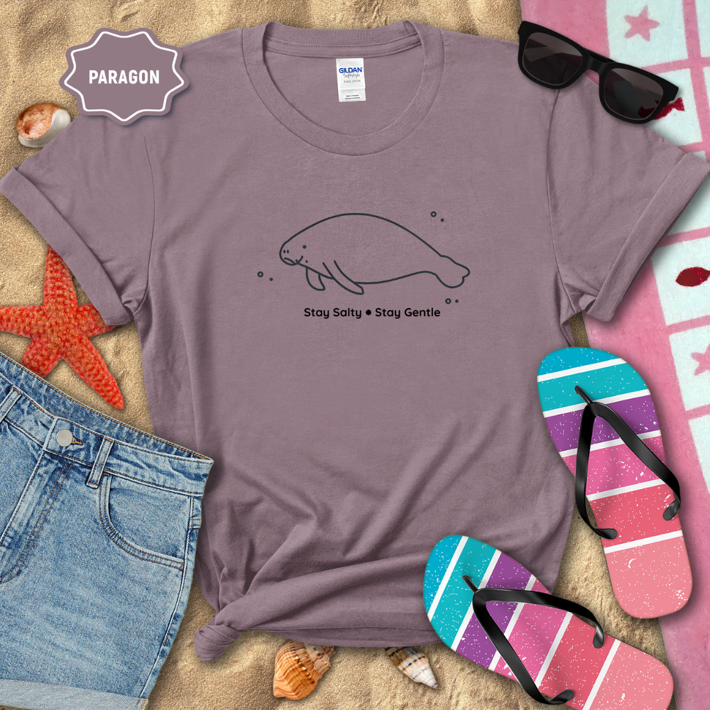 Purple t-shirt with manatee graphic and text 'Stay Salty Stay Gentle' on a sandy background with beach accessories.