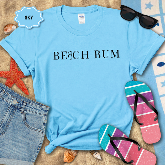 Blue t-shirt with 'BEACH BUM' text on a sandy background with beach accessories.