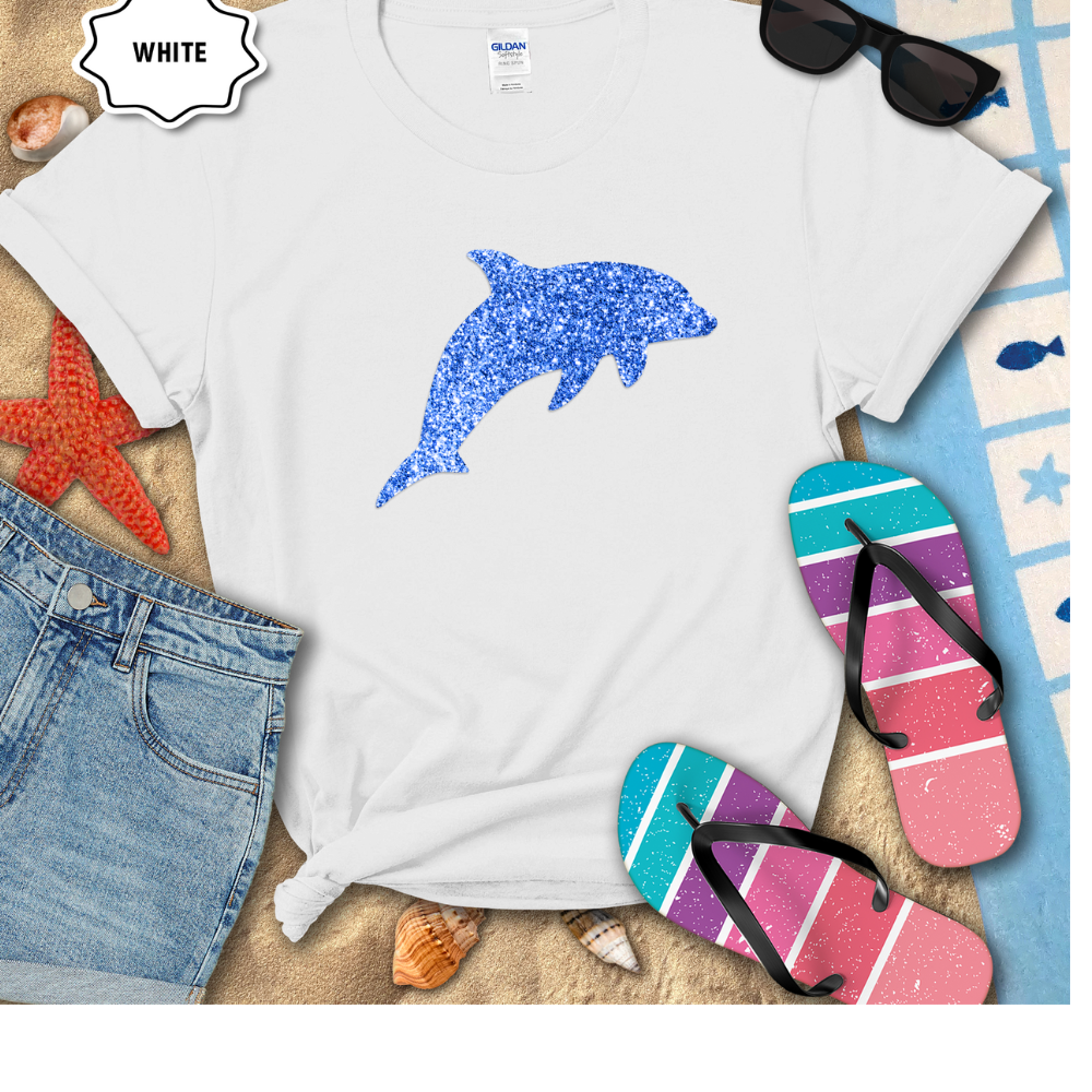 White t-shirt with blue dolphin design on a beach-themed background with flip-flops and sunglasses.