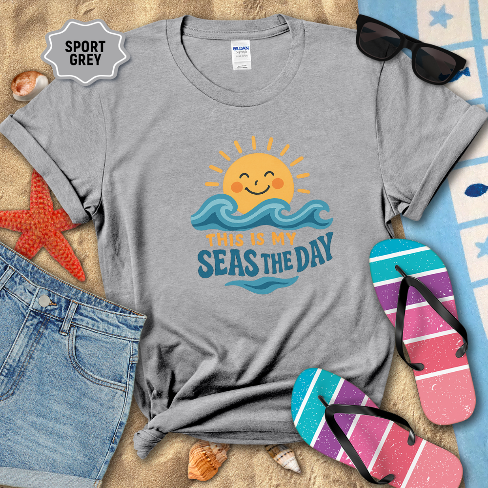 Gray t-shirt with beach-themed design on sand with sunglasses and flip-flops.