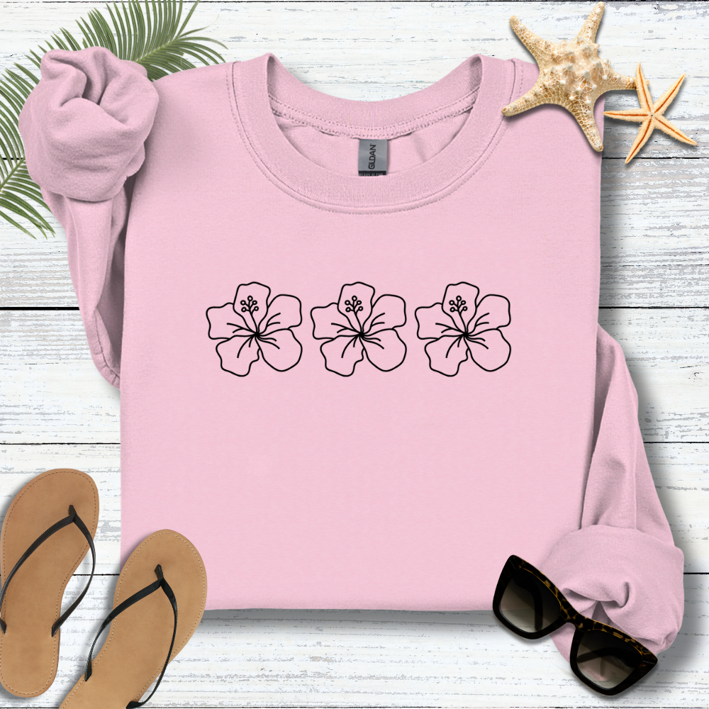 Pink sweatshirt with floral designs on a wooden surface with flip-flops and sunglasses.