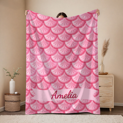 Person holding a pink scalloped patterned blanket with 'Amelia' on it in a room.