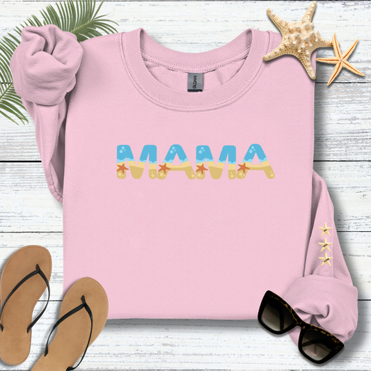 Pink sweatshirt with 'MAMA' text on a wooden surface with beach accessories.
