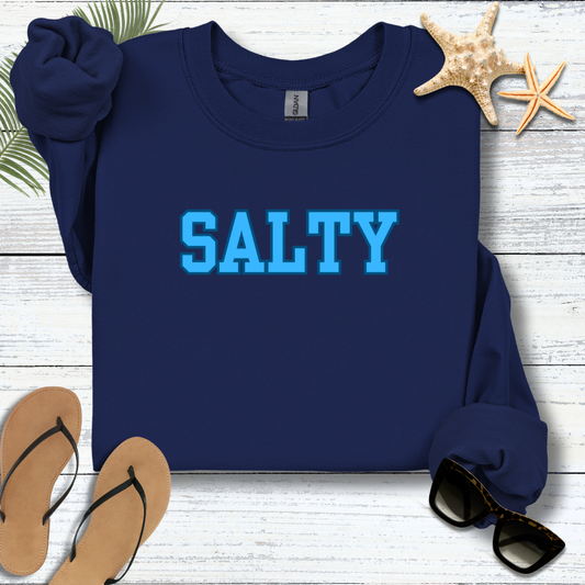 Navy blue sweatshirt with 'SALTY' in blue text on a wooden surface with flip-flops and sunglasses.