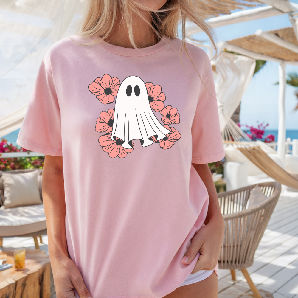 Person wearing a pink t-shirt with a ghost and flower design at a beachside location.