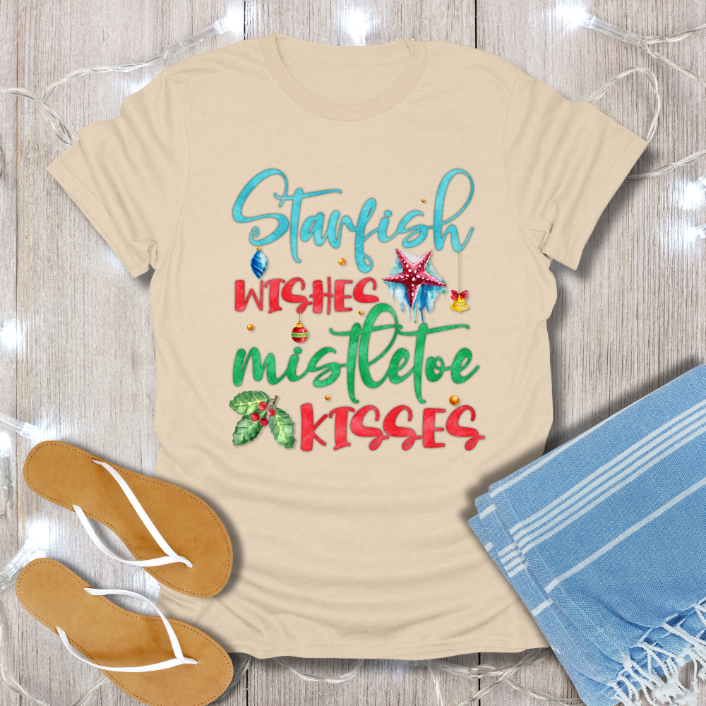 Beige t-shirt with Christmas-themed text and graphics on a wooden surface with flip-flops and a towel.