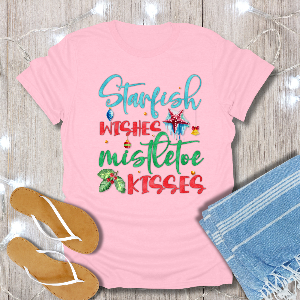 Pink t-shirt with Christmas-themed text on a wooden surface with flip-flops and a towel.