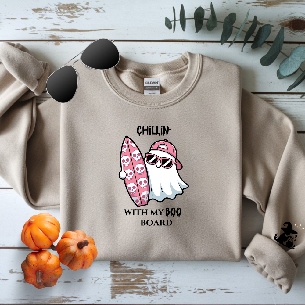 Beige sweatshirt with a ghost holding a Boo Board graphic and text on a wooden surface with pumpkins and leaves.